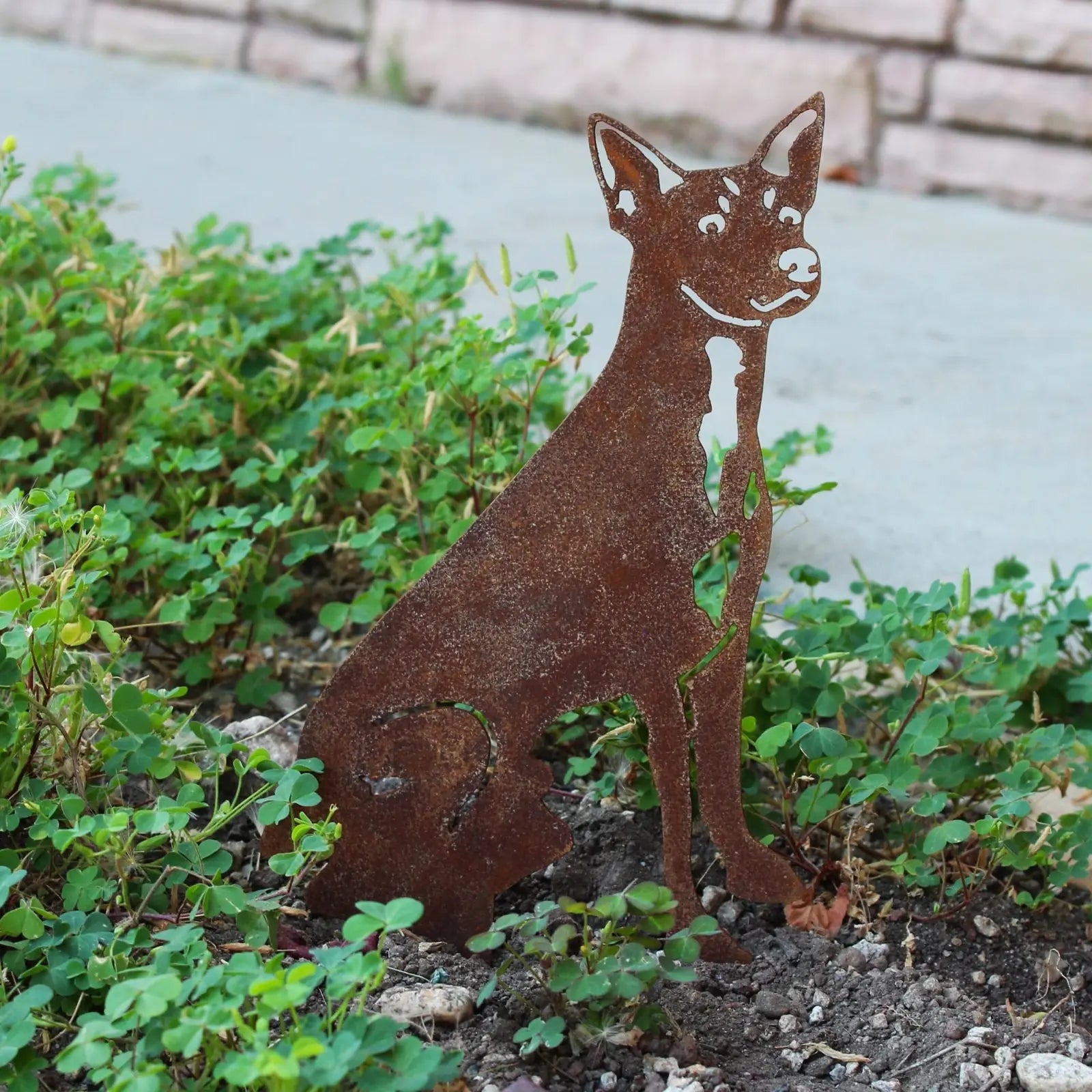 Rust-colored Toy Fox Terrier metal silhouette among greenery, showcasing handcrafted outdoor decor from My Metal Rescue.