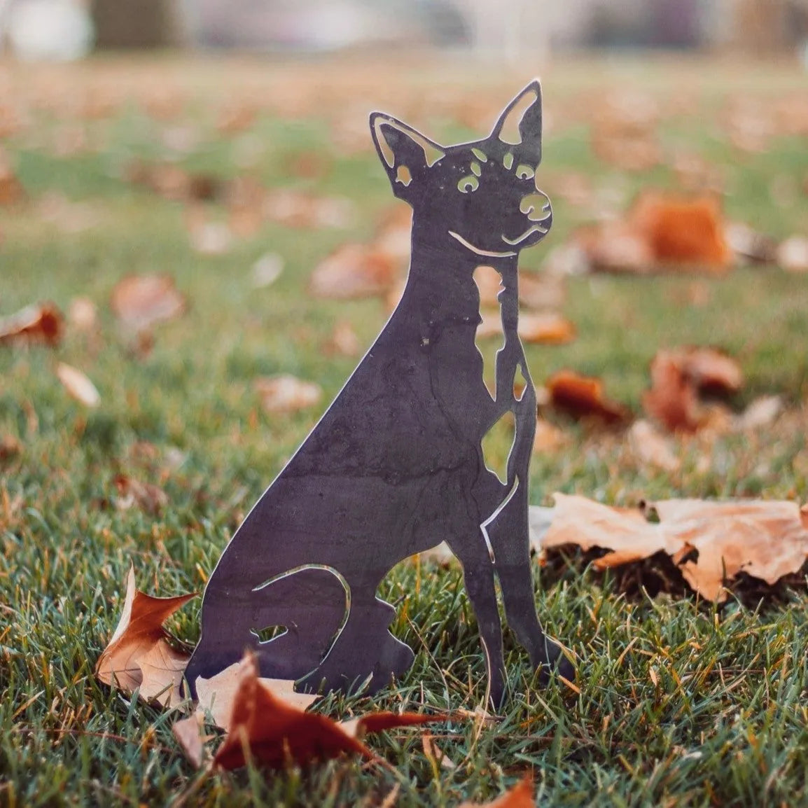 Toy Fox Terrier metal silhouette in matte black, set among fallen leaves on grass, showcasing outdoor dog decor.