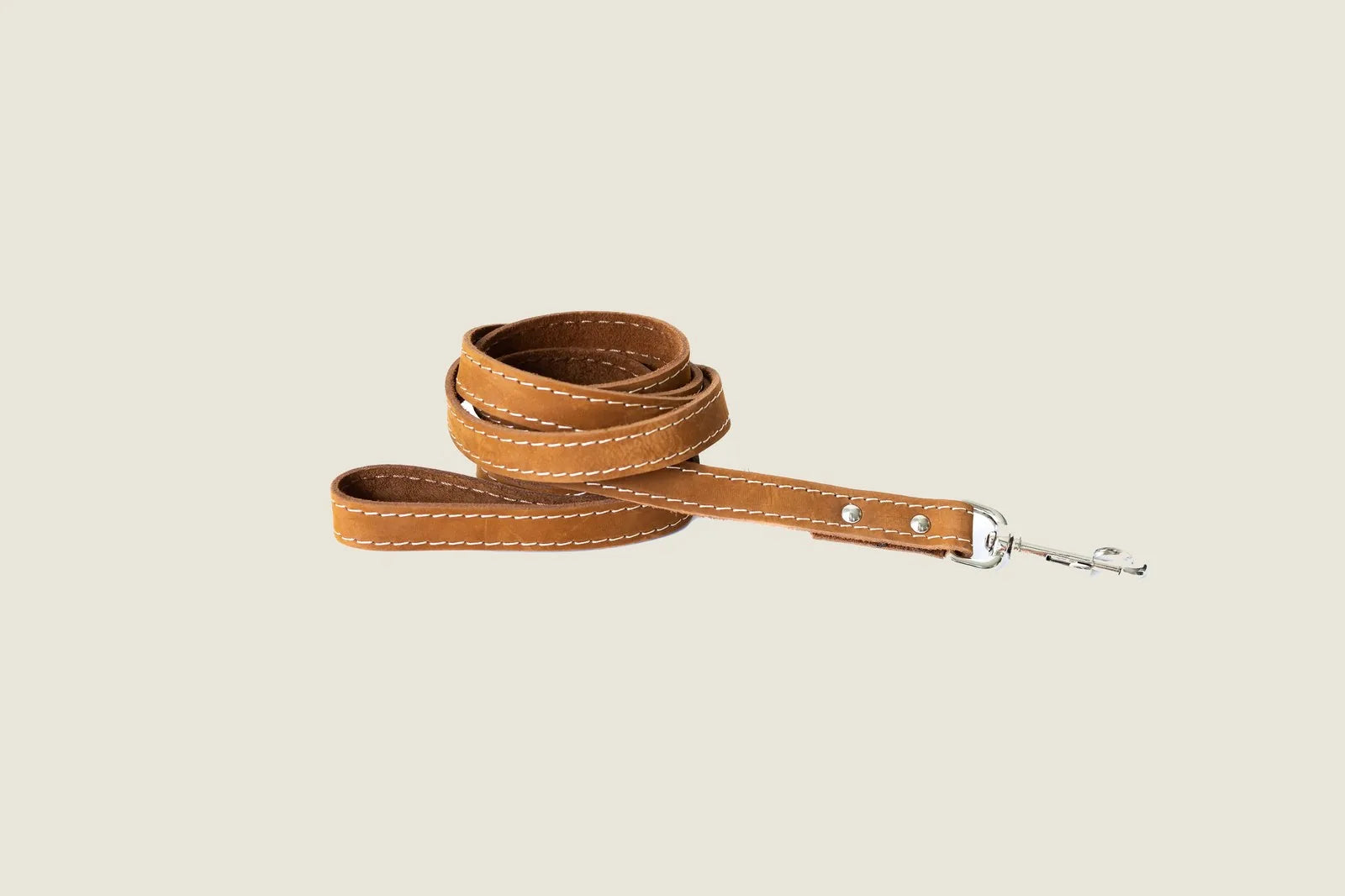 Earth brown leather dog leash with white stitching, featuring European steel hardware, coiled elegantly on a neutral backg...