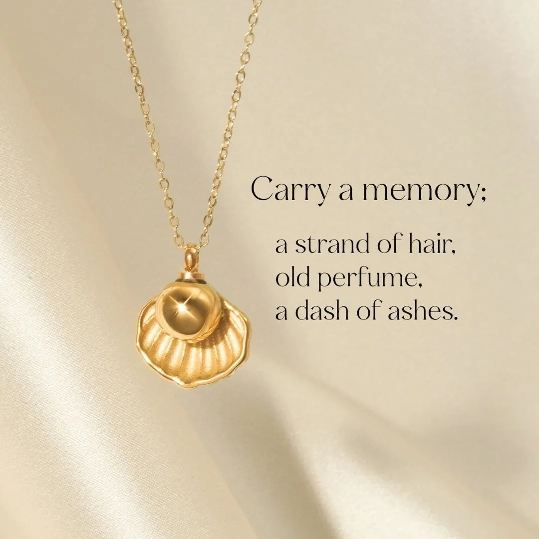 Gold cremation necklace shaped like a shell, designed to hold pet ashes, resting on a light satin background.