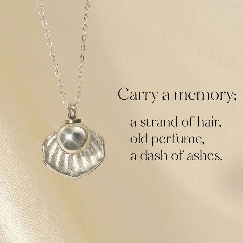 Silver cremation necklace shaped like a shell, featuring a smooth pearl, ideal for holding pet ashes or hair.