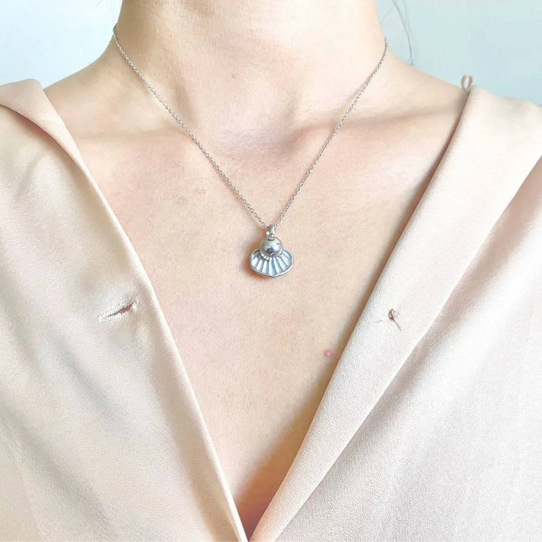 Silver cremation necklace featuring a shell and pearl design, worn elegantly on a delicate chain.