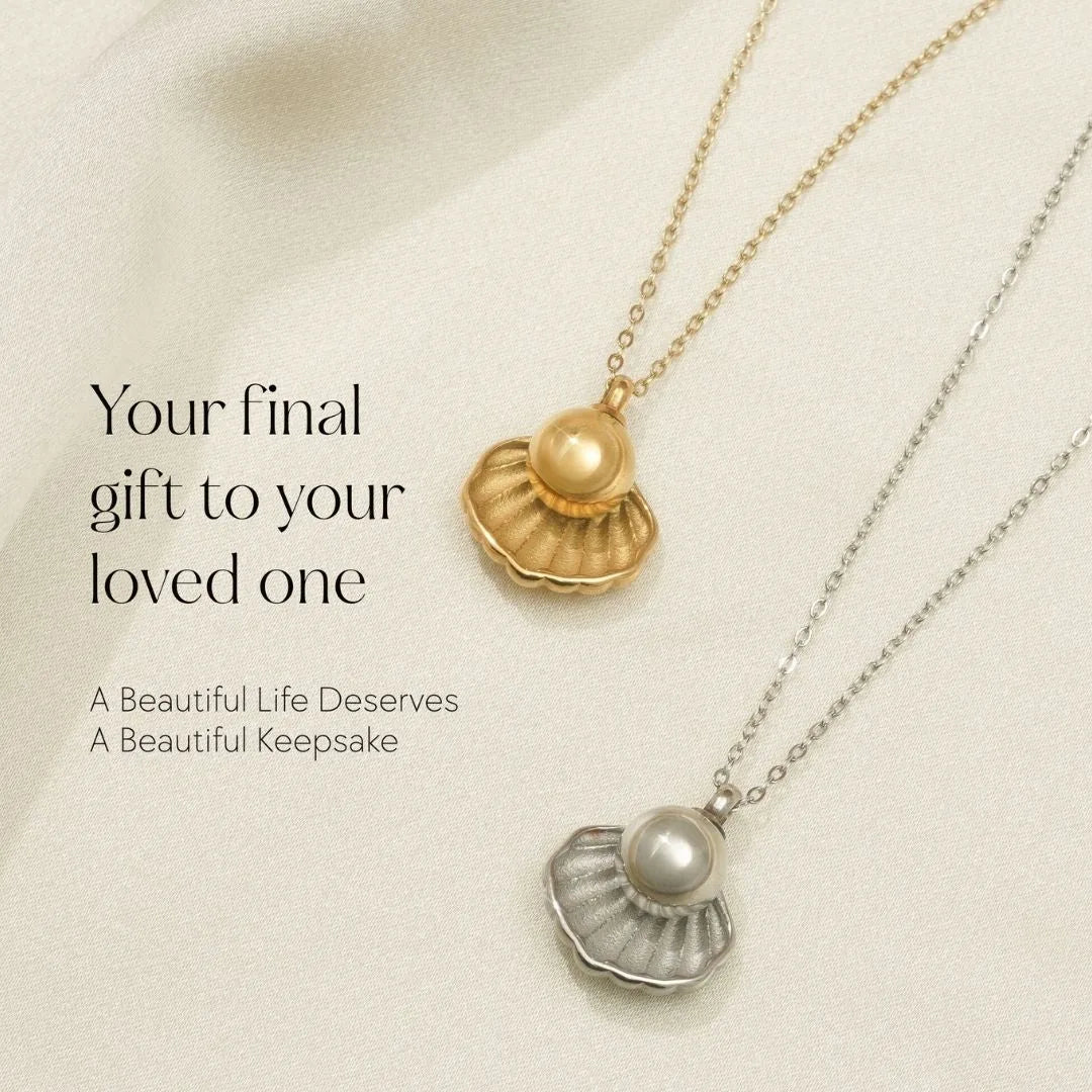Gold and silver memorial necklaces shaped like shells, featuring a pearl, displayed on a soft fabric background.