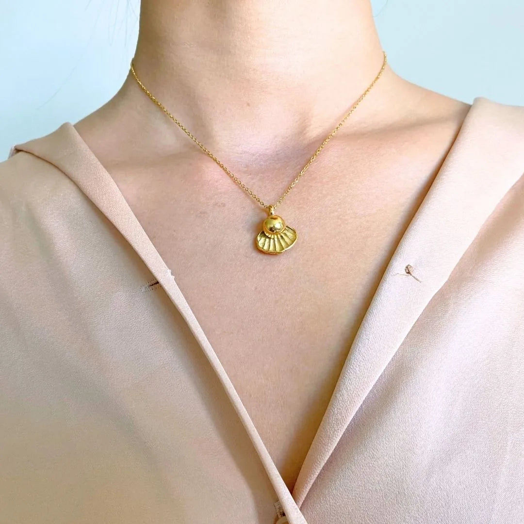 Rose gold memorial necklace with a shell design, worn on a delicate chain, resting against a soft, neutral-toned blouse.