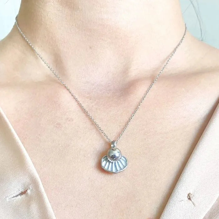 Silver shell-shaped memorial necklace with a pearl centerpiece, worn on a delicate chain.