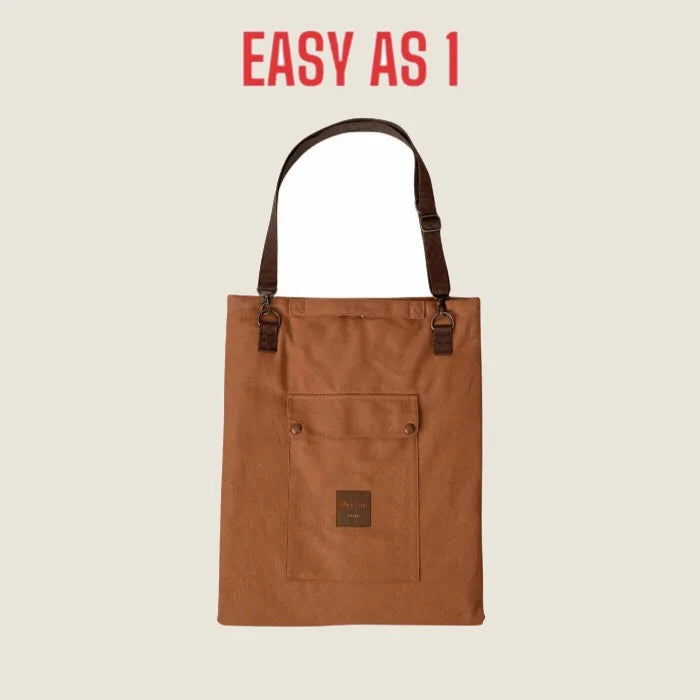 Portable brown canvas mat with a front pocket and adjustable strap, designed for travel with dogs and humans.