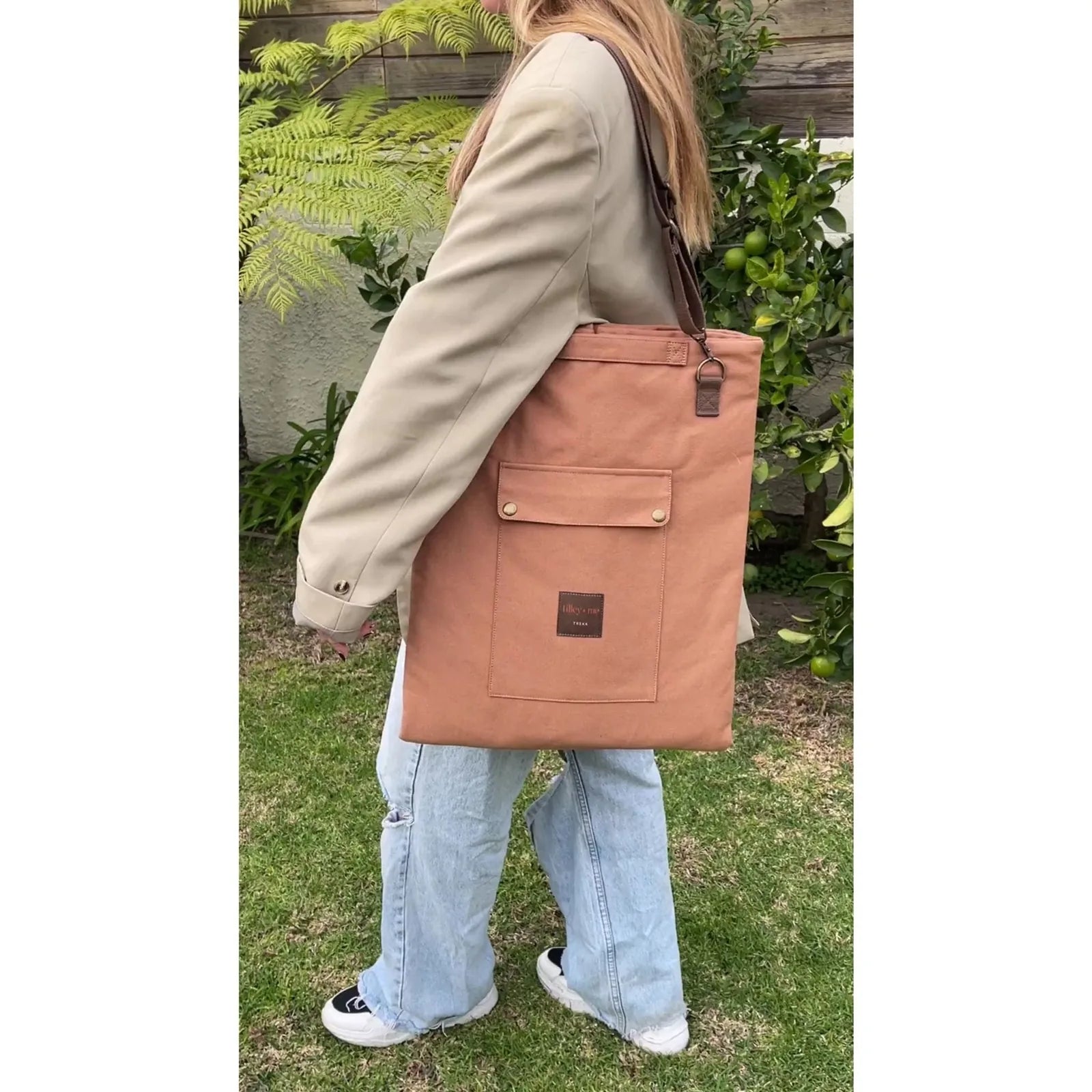 Convertible canvas mat in burnt orange worn as a messenger bag, featuring a front pocket and adjustable strap.