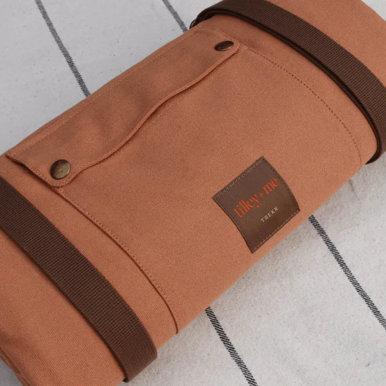 Portable orange canvas mat rolled up, featuring brown straps and a leather label, perfect for outdoor adventures.