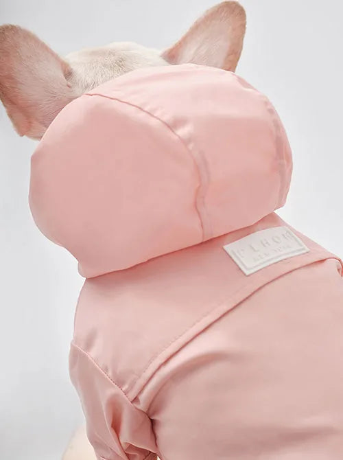 Light pink adjustable raincoat for dogs, featuring a hood and velcro closures, designed for easy wear and comfort.