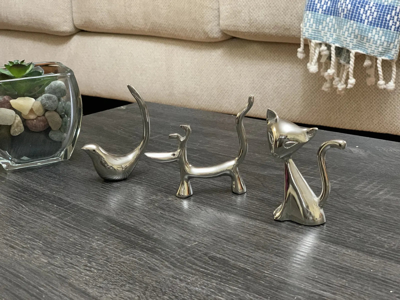 Glossy silver dog, cat, and bird ring holders set on a dark wood table, showcasing modern collectible design.