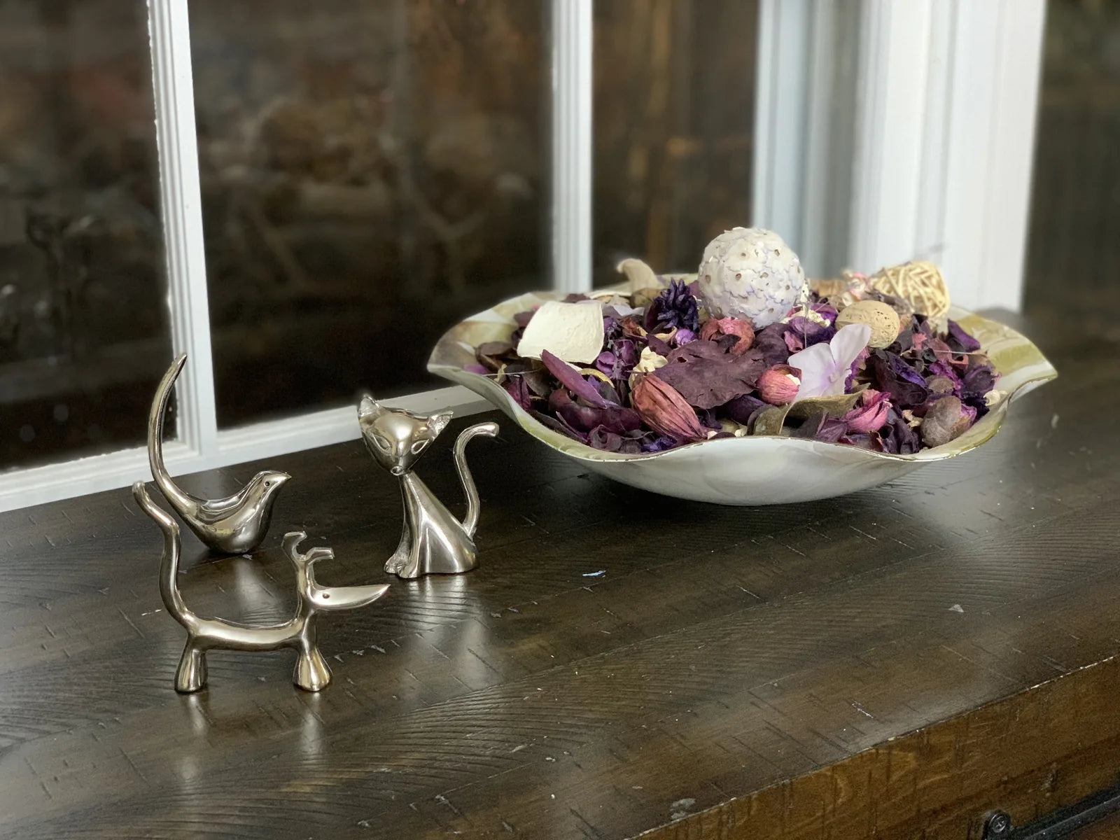 Glossy silver dog, cat, and bird ring holders displayed on a wooden surface, surrounded by decorative potpourri.