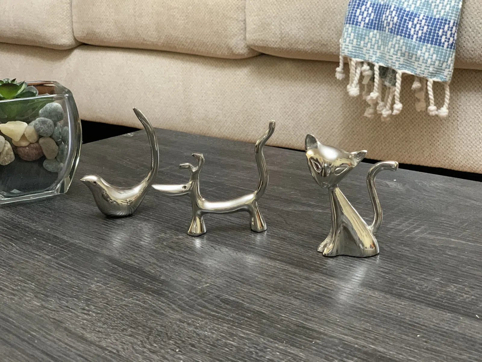 Glossy silver ring holders shaped like a dog, cat, and bird, elegantly displayed on a dark wooden surface.