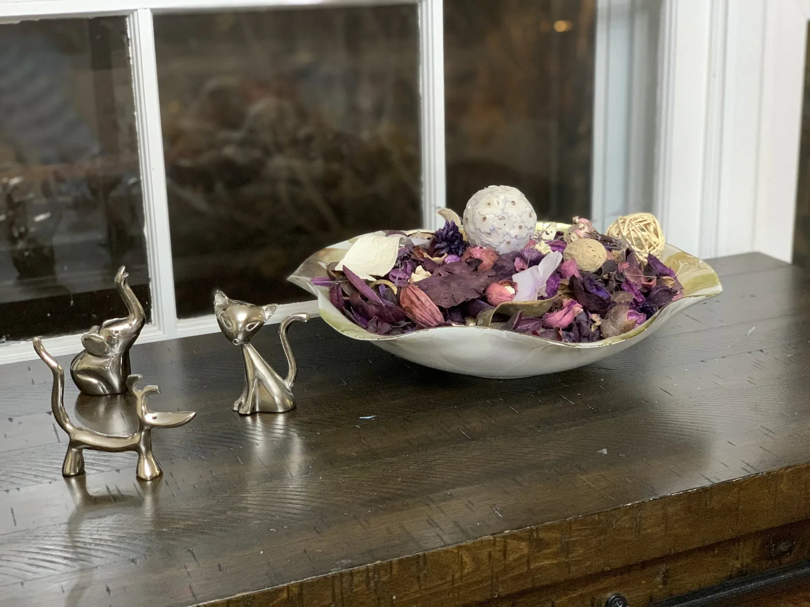 Glossy silver ring holders shaped like a dog, cat, and elephant, displayed on a wooden table with decorative potpourri.