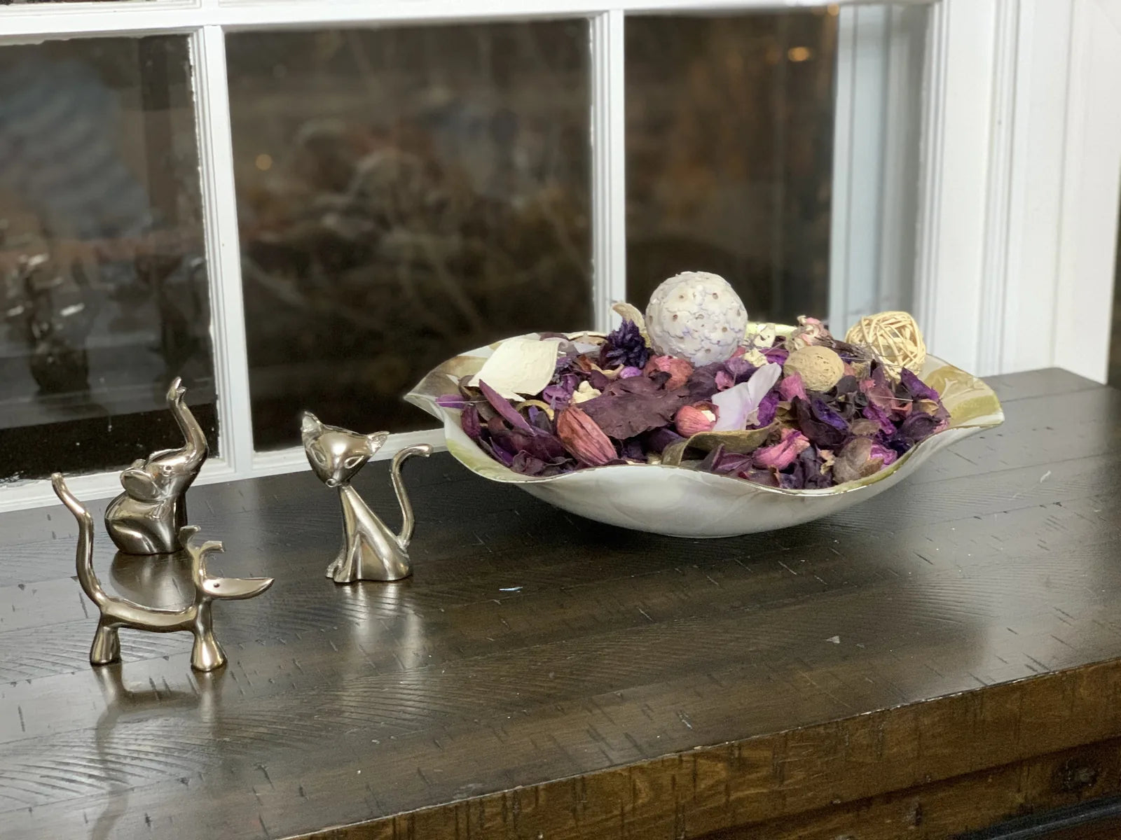 Silver dog, cat, and elephant ring holders displayed on a dark wooden table with decorative dried flowers.