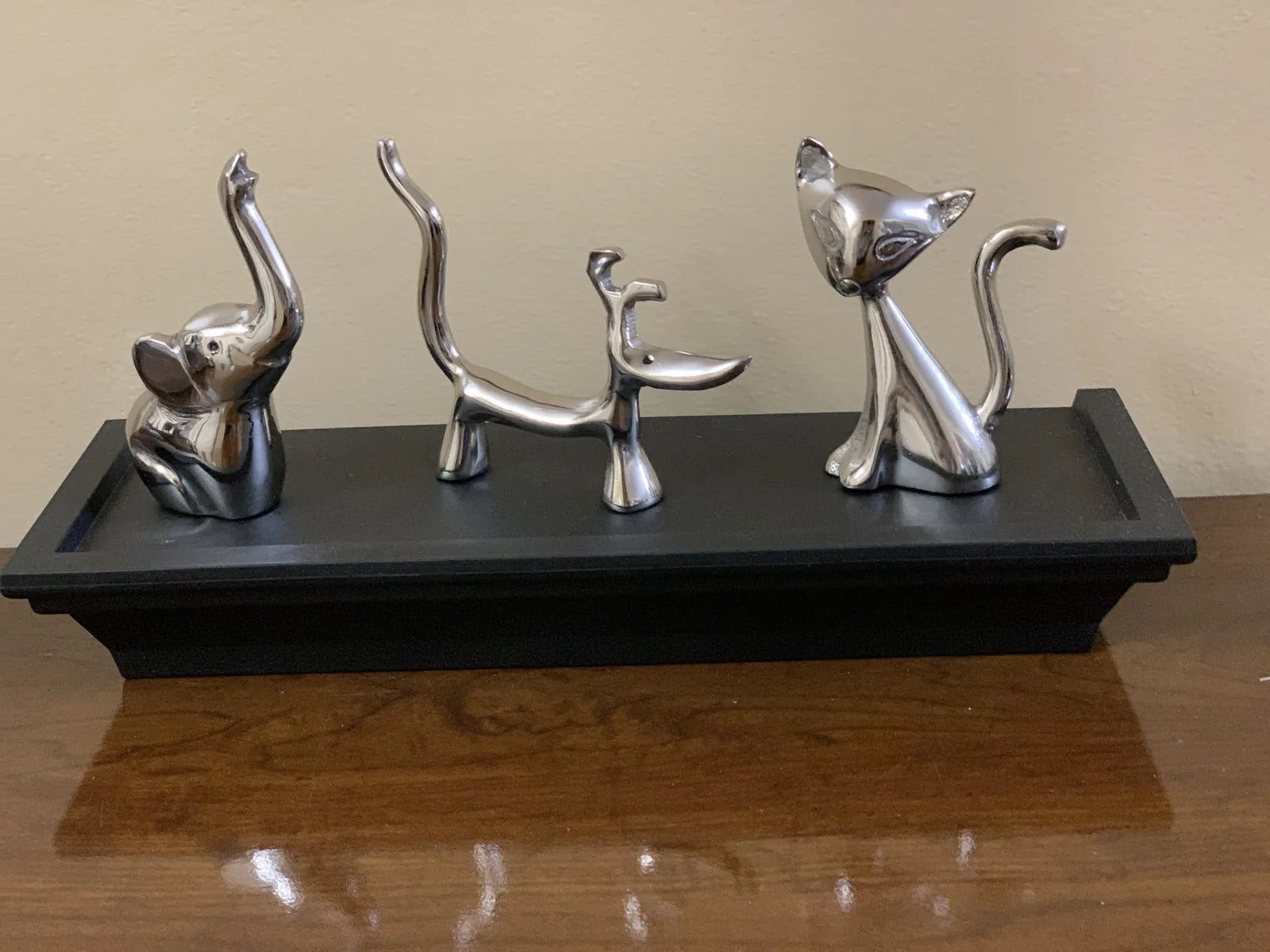 Glossy silver ring holders shaped like a dog, cat, and elephant placed on a black display base.