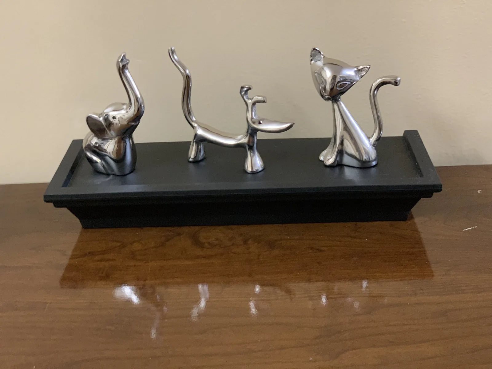 Set of three shiny silver ring holders shaped like a dog, cat, and elephant on a black display tray.