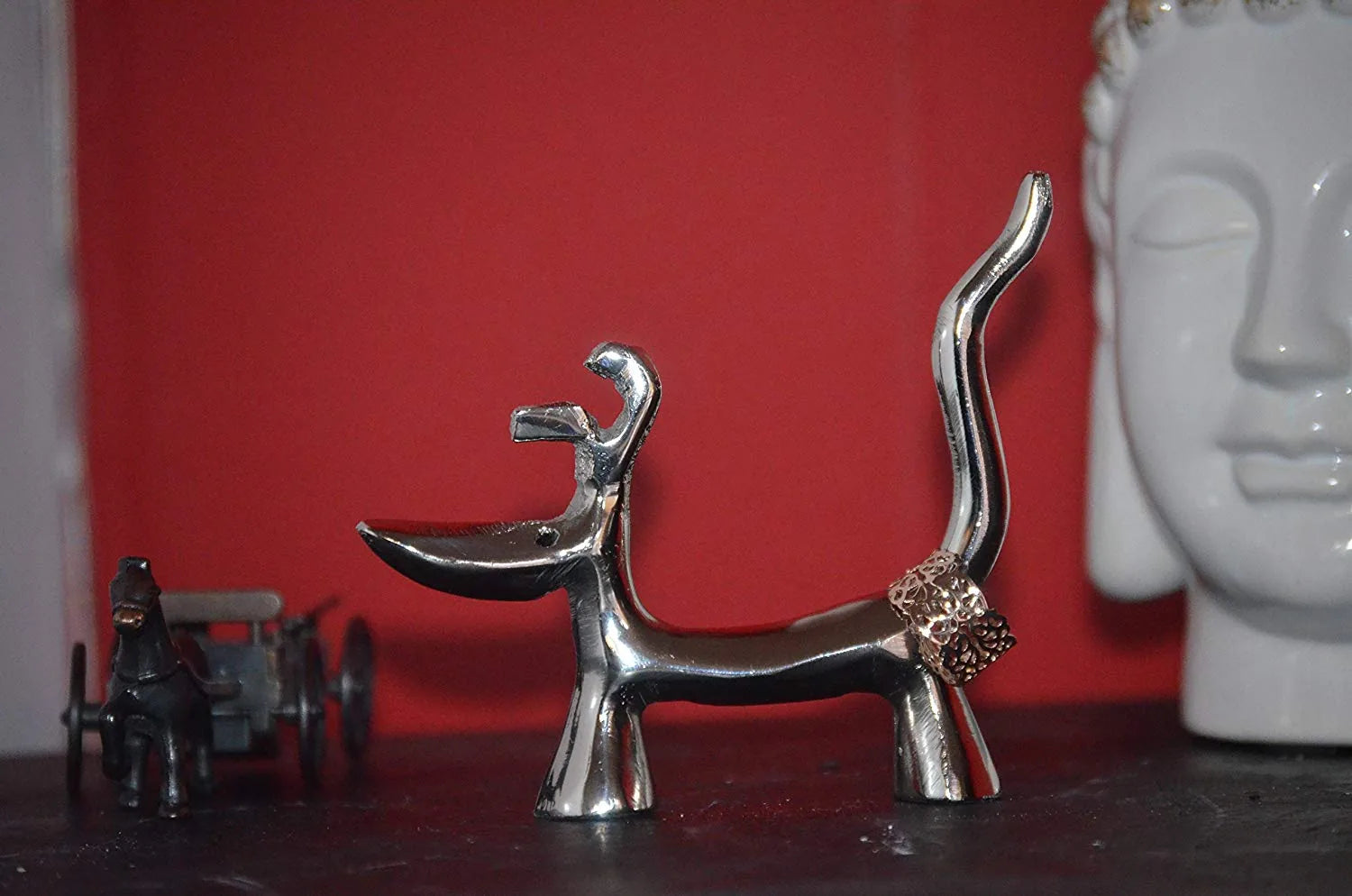 Handcrafted silver dog-shaped ring holder, featuring a decorative ring, against a red background.