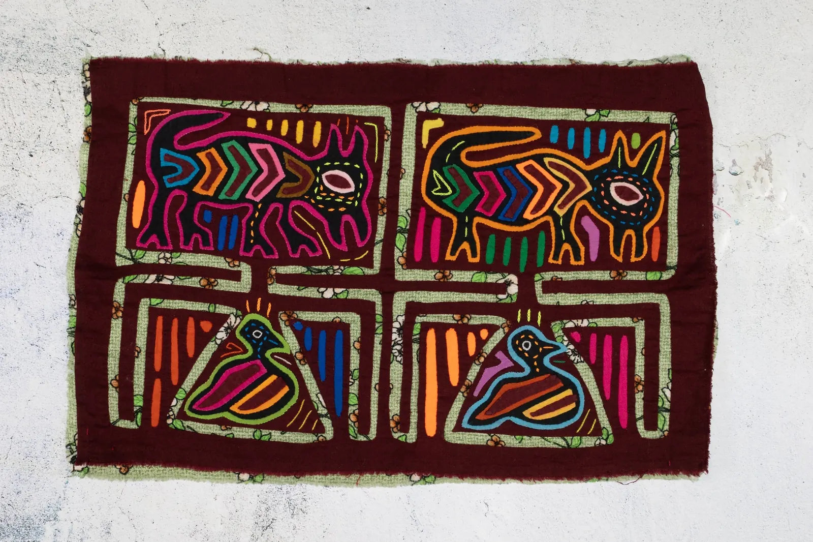 Hand-stitched Mola featuring colorful vintage bird and puppy dog designs against a rich maroon background.