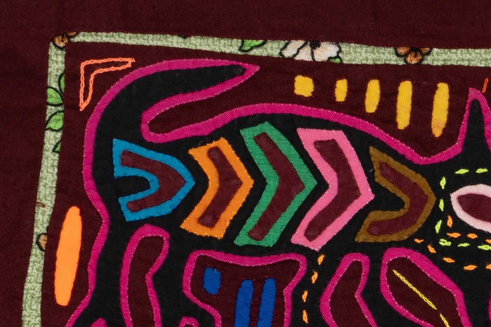 Close-up of a hand-stitched Mola featuring vibrant bird and puppy motifs in bright colors against a maroon background.