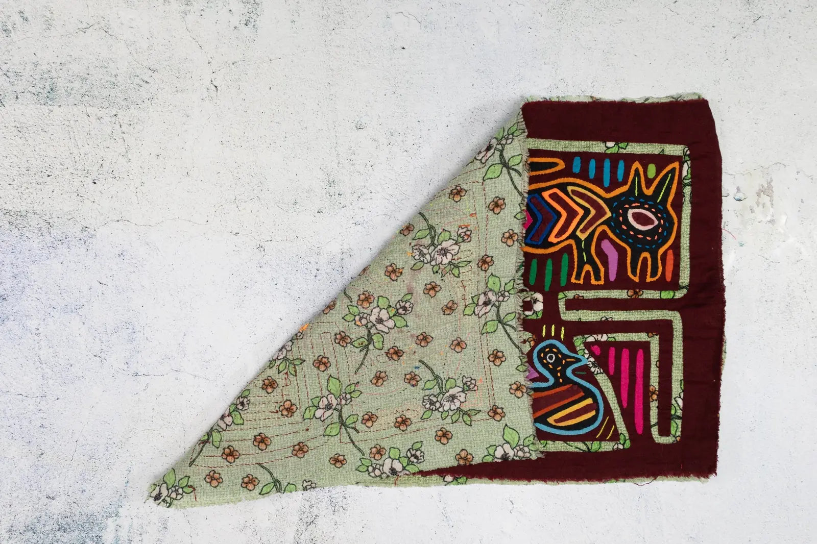 Hand-stitched vintage Mola showing a colorful puppy and bird on a floral green background, highlighting intricate textile...
