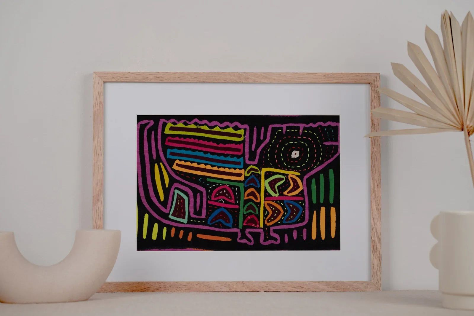 Colorful vintage black and purple Mola featuring geometric patterns, framed and displayed with a minimalist vase.