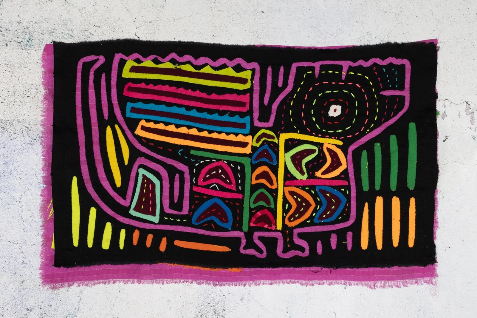Colorful hand-stitched Mola tapestry featuring a geometric puppy design in vivid purple, green, and orange on a black back...