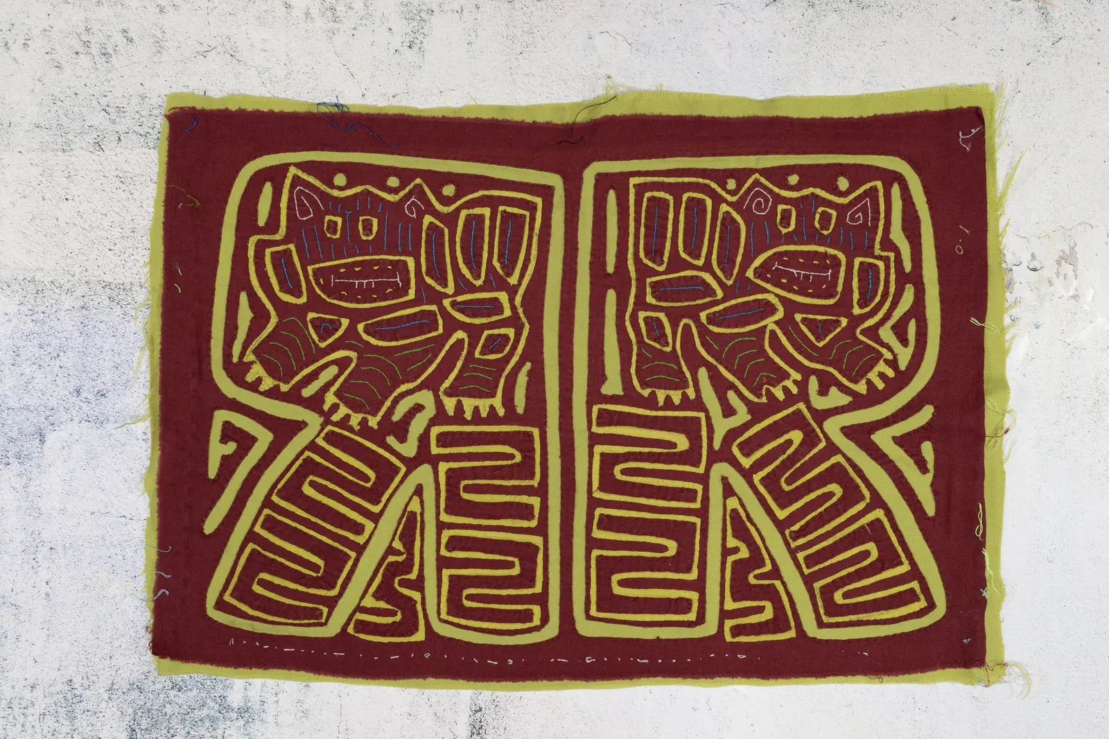 Hand-stitched vintage mola tapestry featuring playful pup designs in burgundy and green, showcasing geometric patterns.