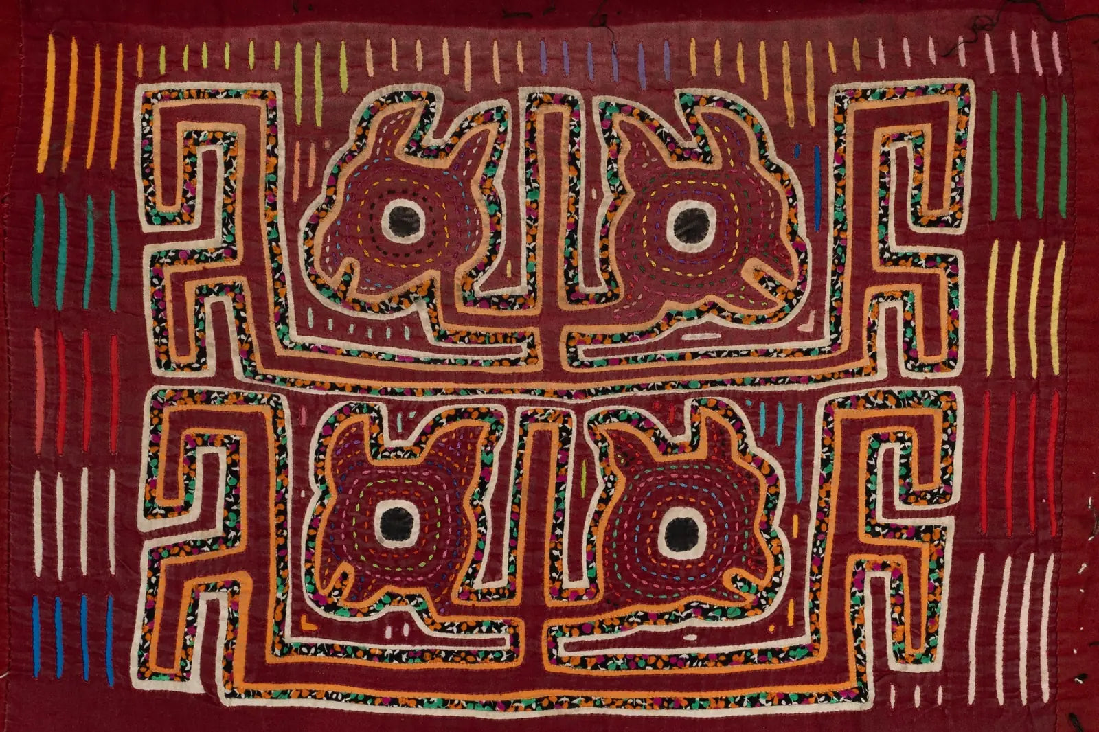 Burgundy hand-stitched Mola featuring playful puppy designs surrounded by colorful patterns, showcasing traditional Panama...