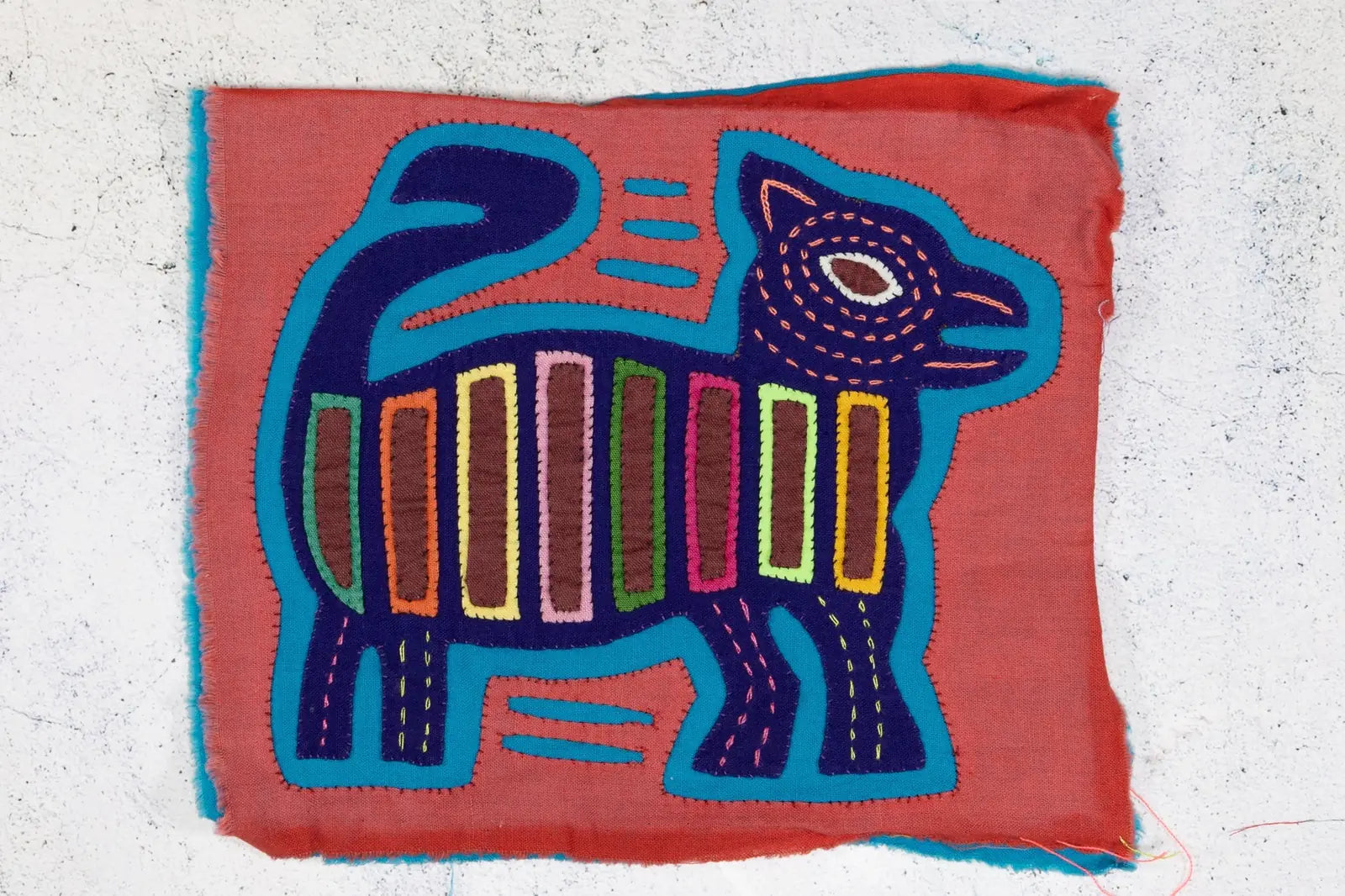 Hand-stitched vintage pink and purple Mola featuring a decorative dog design with bright geometric patterns.
