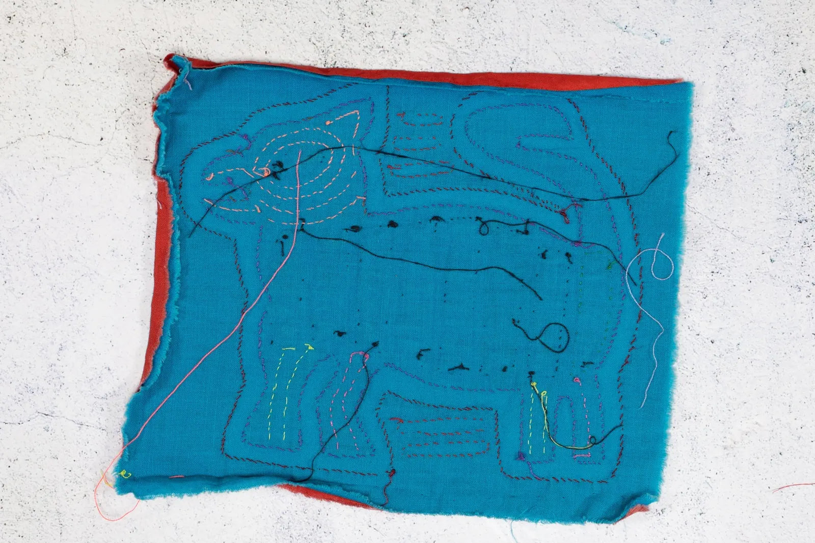 Vibrant turquoise fabric featuring a hand-stitched dog design, highlighted with colorful embroidery threads.