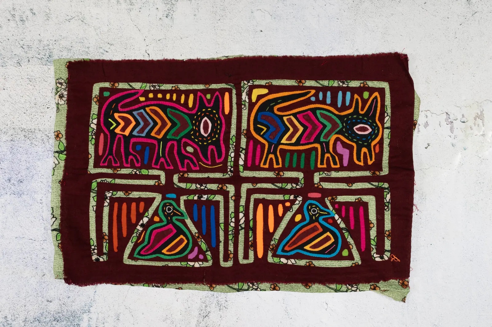 Colorful hand-stitched tapestry featuring a puppy and bird design on a dark burgundy background.