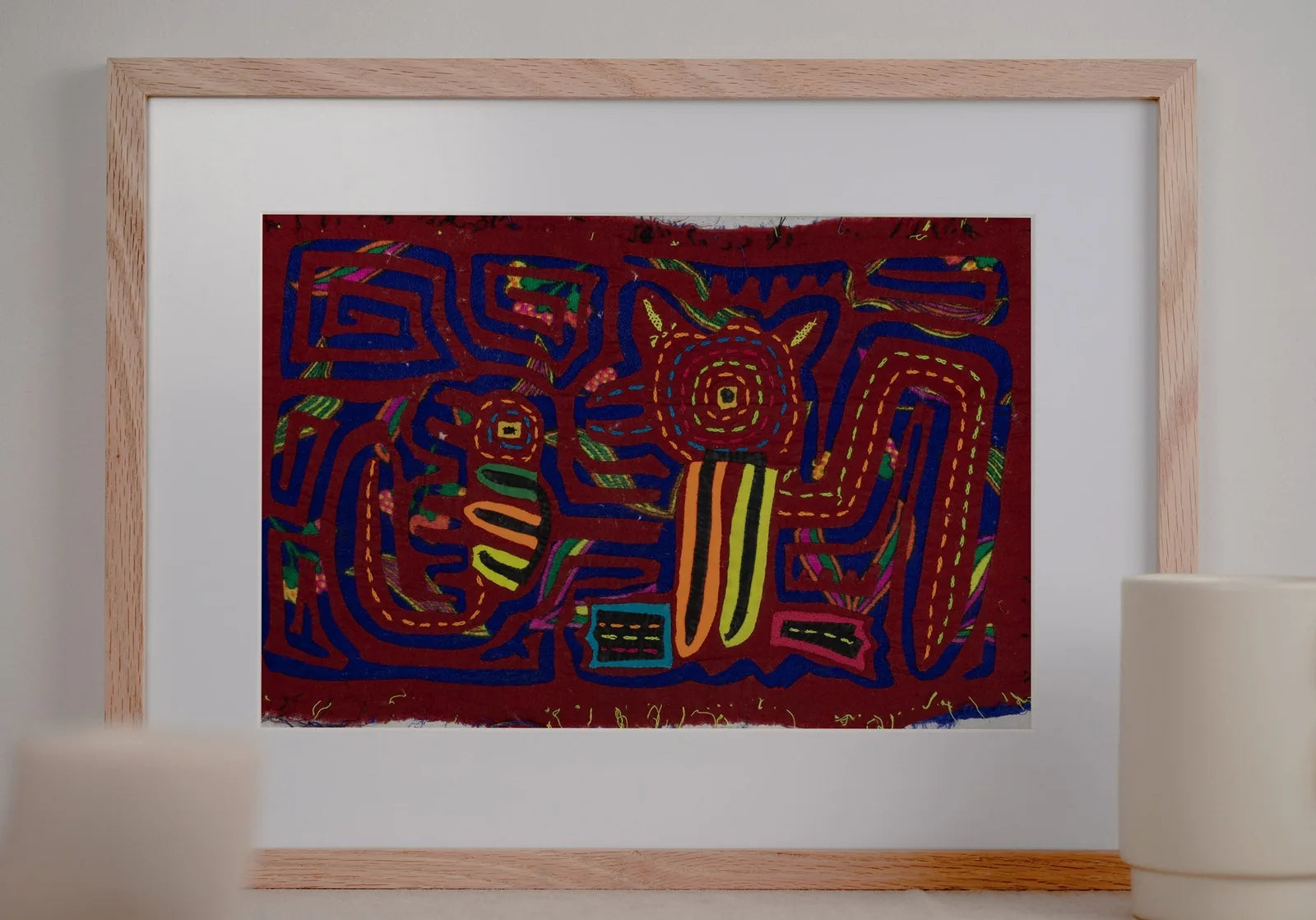 Hand-stitched Panama Mola featuring vibrant geometric patterns of a puppy and gecko on deep red fabric.