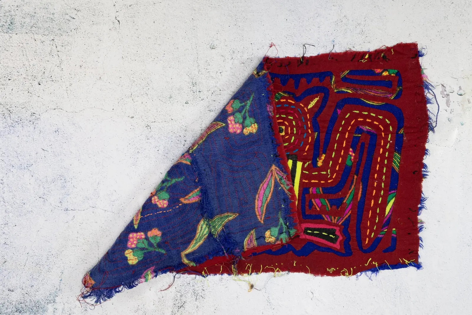 Hand-stitched Panama Mola featuring vibrant red and blue colors, showcasing floral and geometric designs.