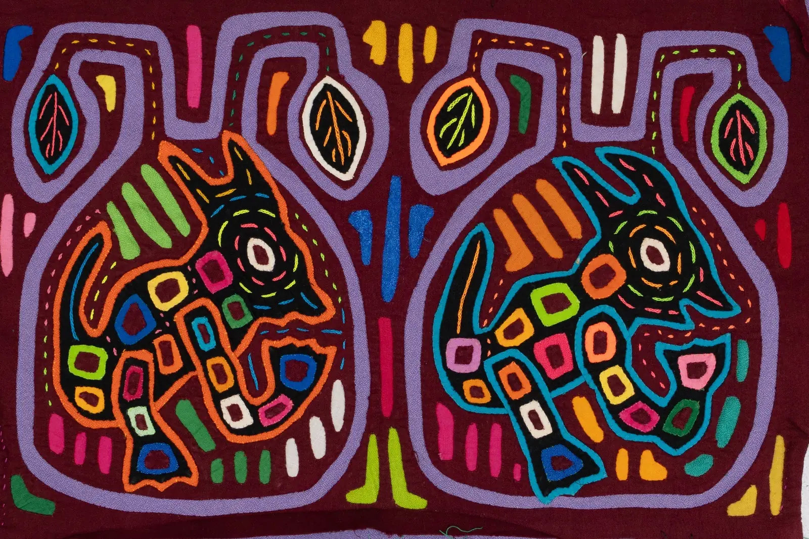 Colorful hand-stitched Mola tapestry featuring two playful dog designs against a maroon background, highlighting Latin Ame...
