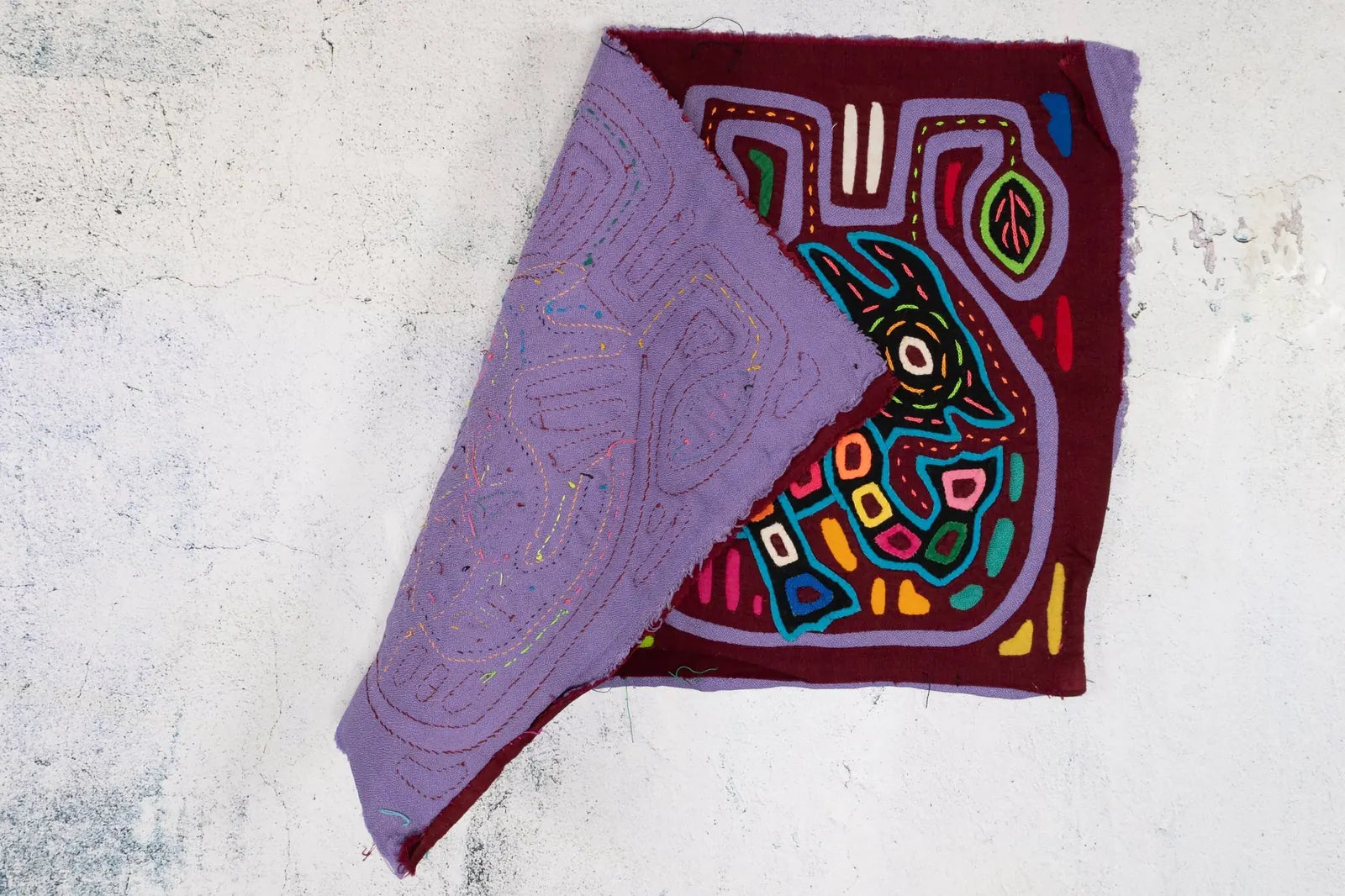 Colorful hand-stitched Mola tapestry featuring a vibrant dog design on a maroon background, showcasing intricate textile art.