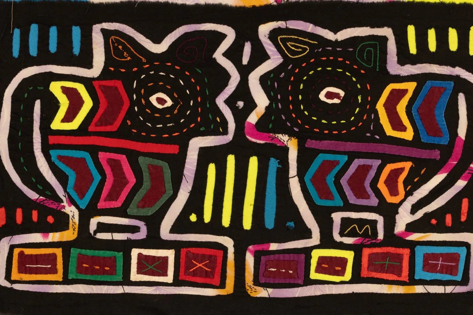 Colorful hand-stitched vintage mola tapestry featuring two puppy dog figures in geometric patterns against a black backgro...