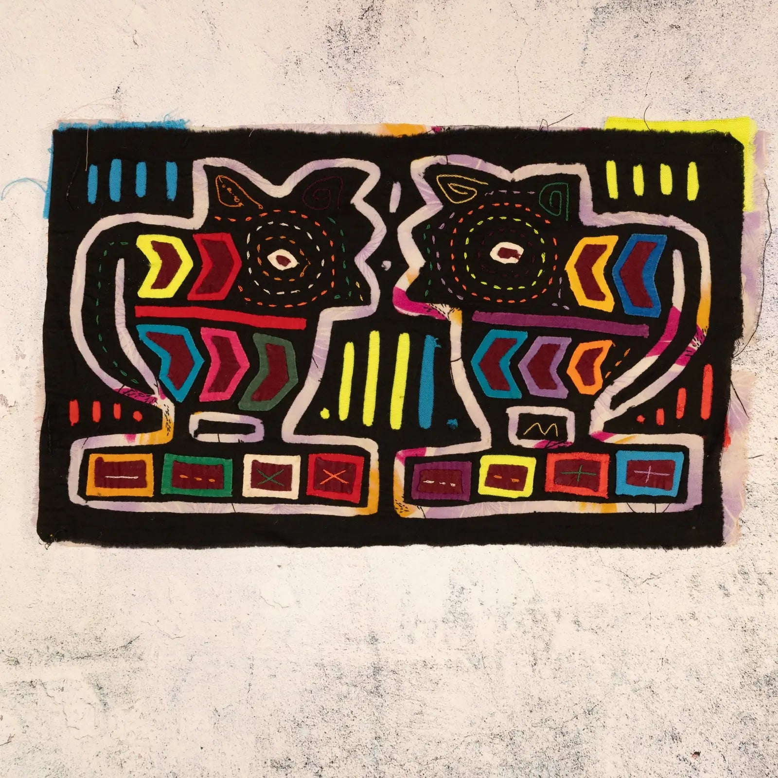 Colorful hand-stitched mola depicting two smiling puppies against a black background, showcasing geometric patterns in vib...