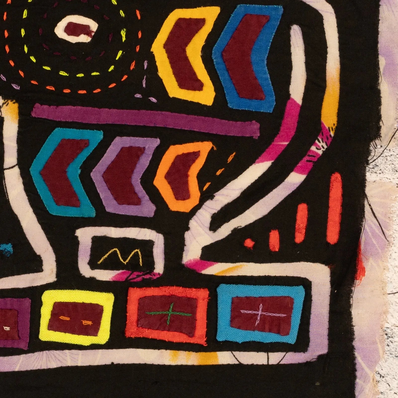 Colorful hand-stitched vintage Mola featuring geometric shapes and bold patterns on a black background.