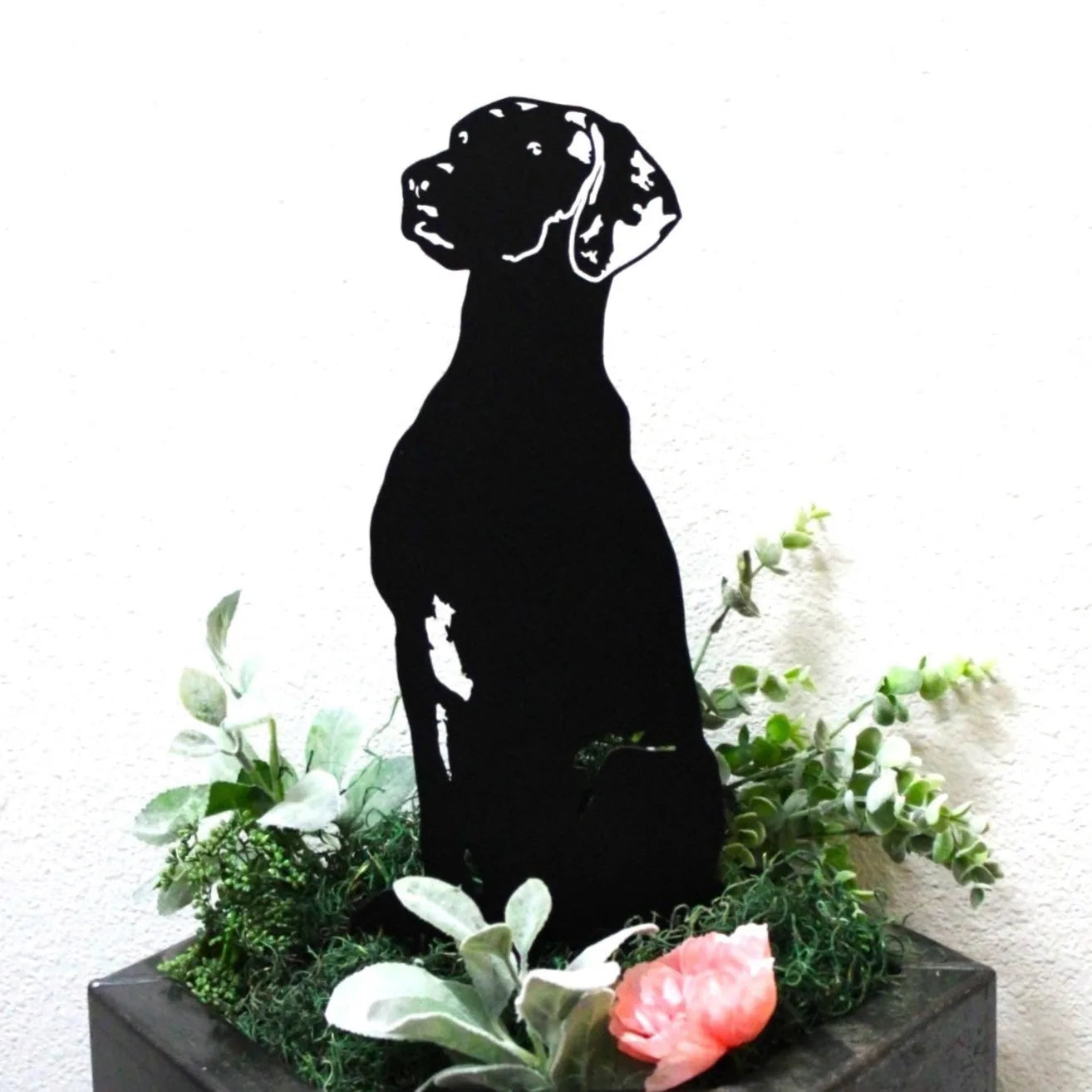 Black metal Vizsla silhouette sitting among green foliage and pink flowers, showcasing durable outdoor dog decor.