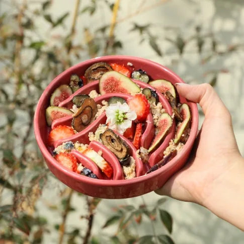 Bright pink slow feeder dog bowl filled with fruit, held in hand against a blurred green background.