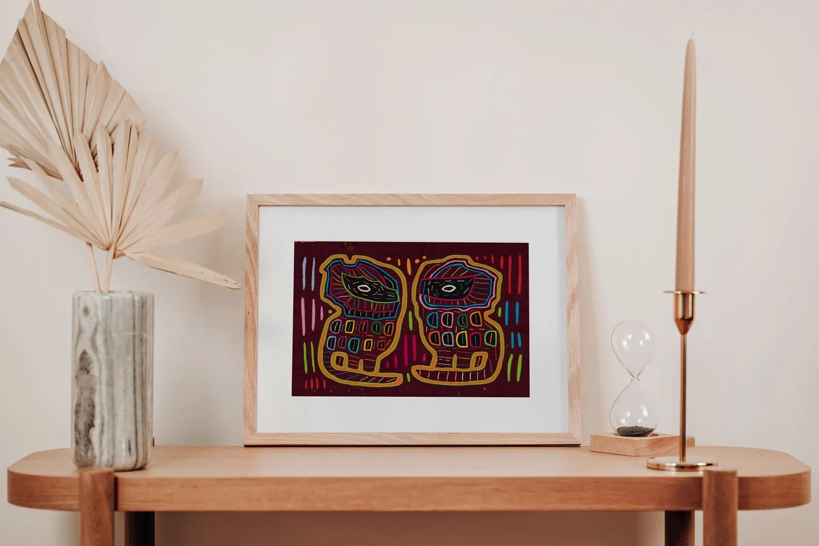 Colorful Molas tapestry featuring two stylized dogs with geometric patterns, framed and displayed on a wooden shelf.