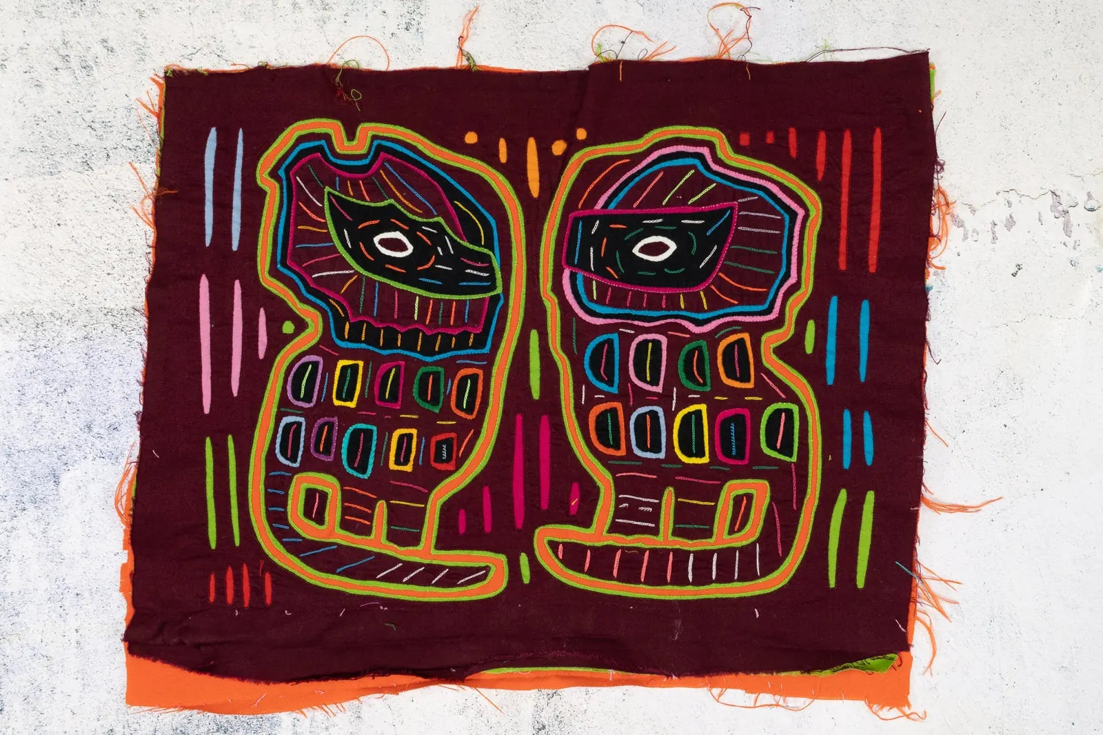 Colorful hand-stitched Mola tapestry featuring two abstract dog figures on a burgundy background with geometric patterns.