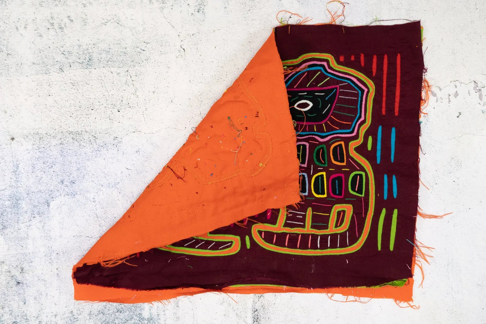Colorful hand-stitched fabric tapestry showing vibrant patterns in orange and maroon, showcasing traditional Guna artistry.