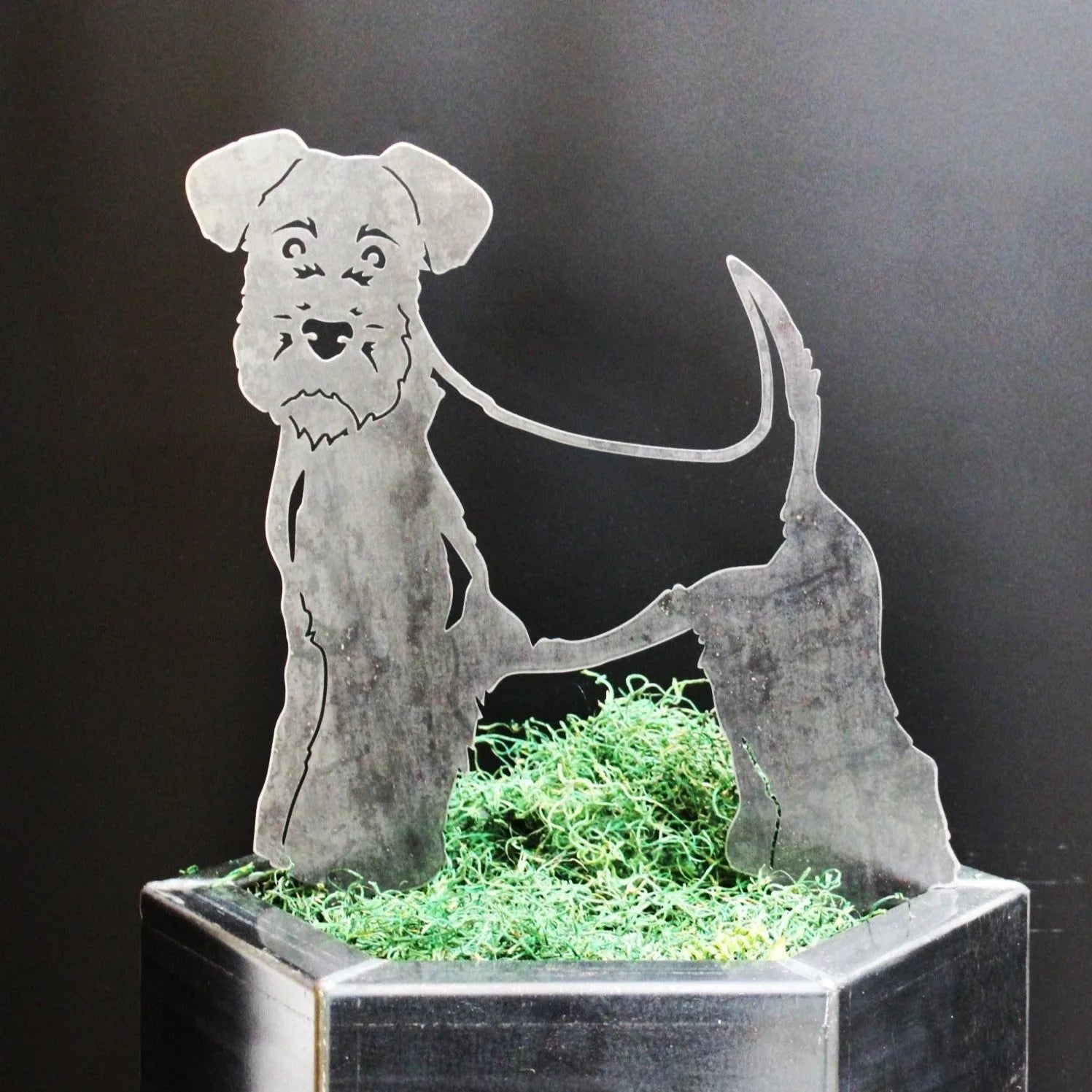 Welsh Terrier metal silhouette in rustic Corten steel, showcasing intricate detailing and standing amidst green moss.
