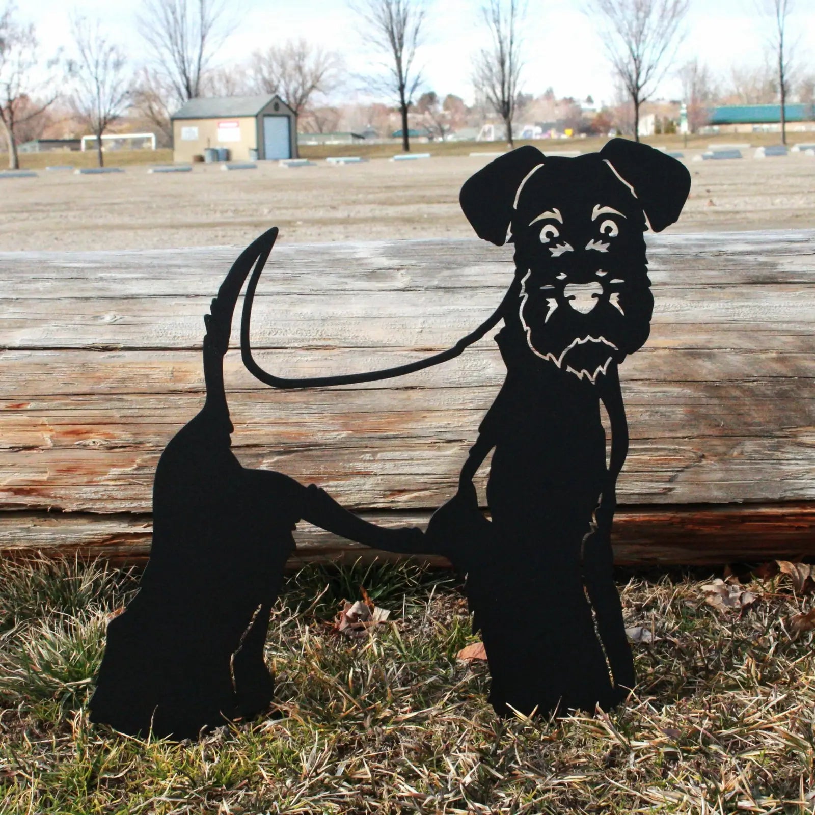 Black metal silhouette of a Welsh Terrier standing in grass, showcasing its features and leash design against a rustic bac...