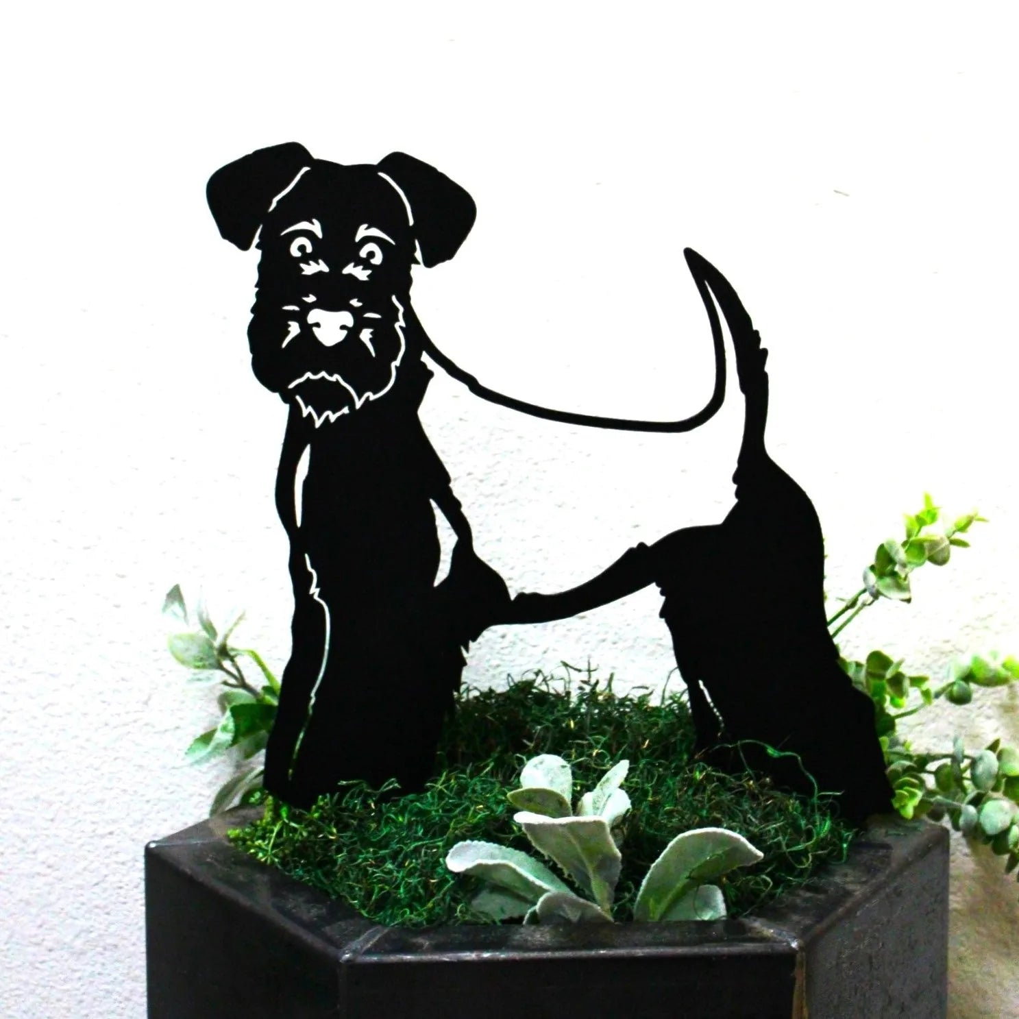 Welsh Terrier metal silhouette in matte black, showcasing detailed features, nestled in green foliage decor.