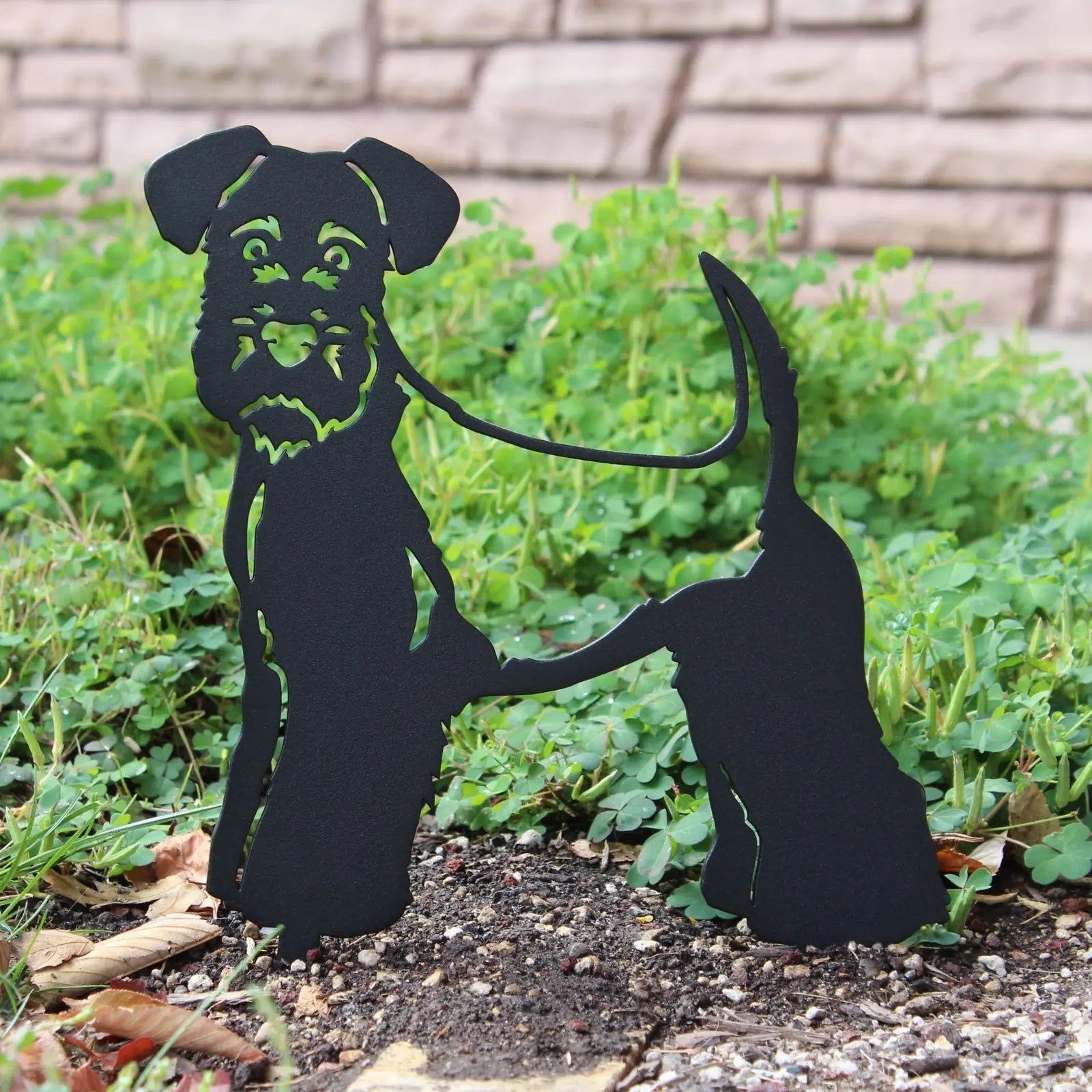 Black metal silhouette of a Welsh Terrier standing in a garden, showcasing a playful design with detailed features.