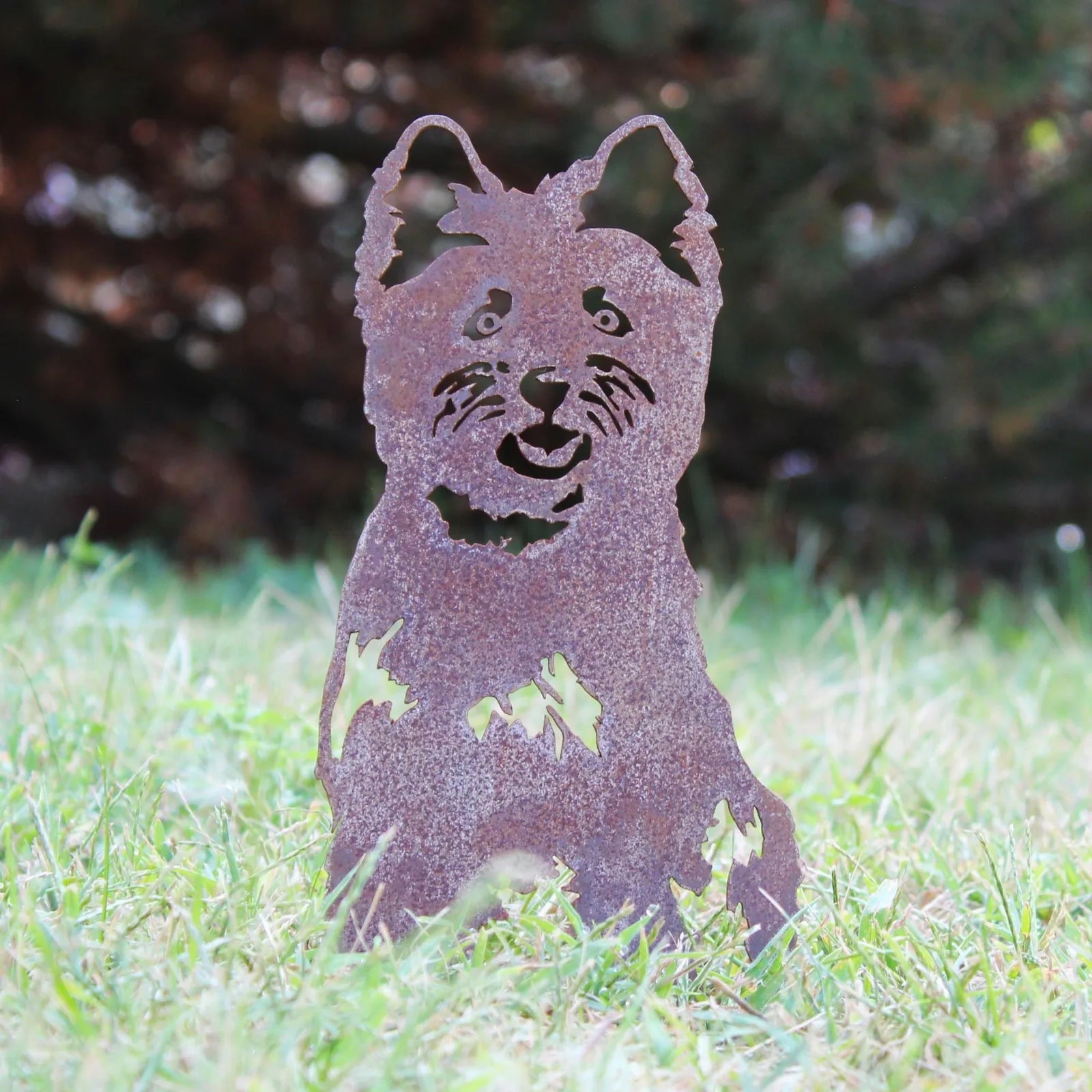 Rusty Corten steel silhouette of a West Highland White Terrier, set in grassy outdoor decor.
