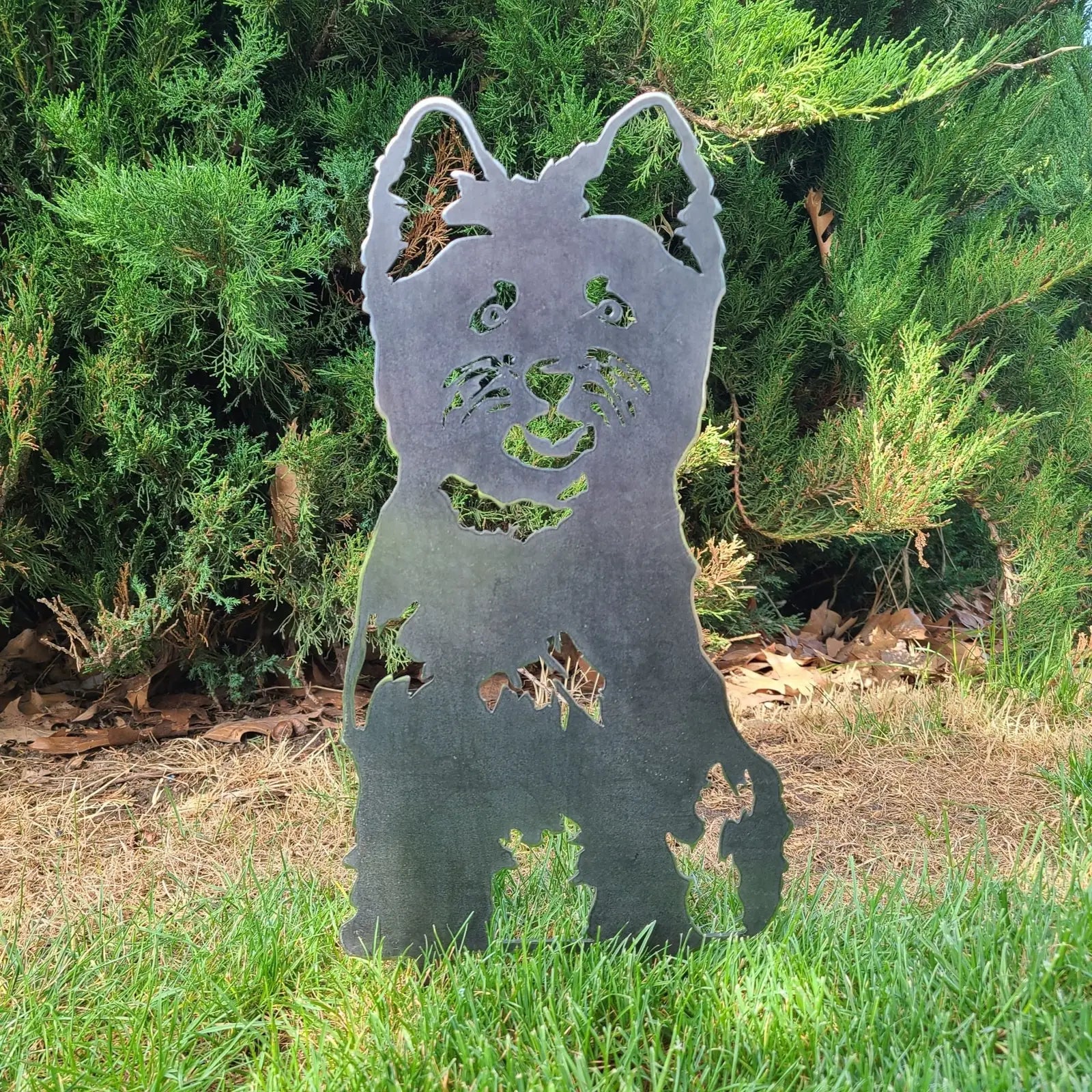 West Highland White Terrier metal silhouette in weathered steel, standing among greenery in a garden setting.