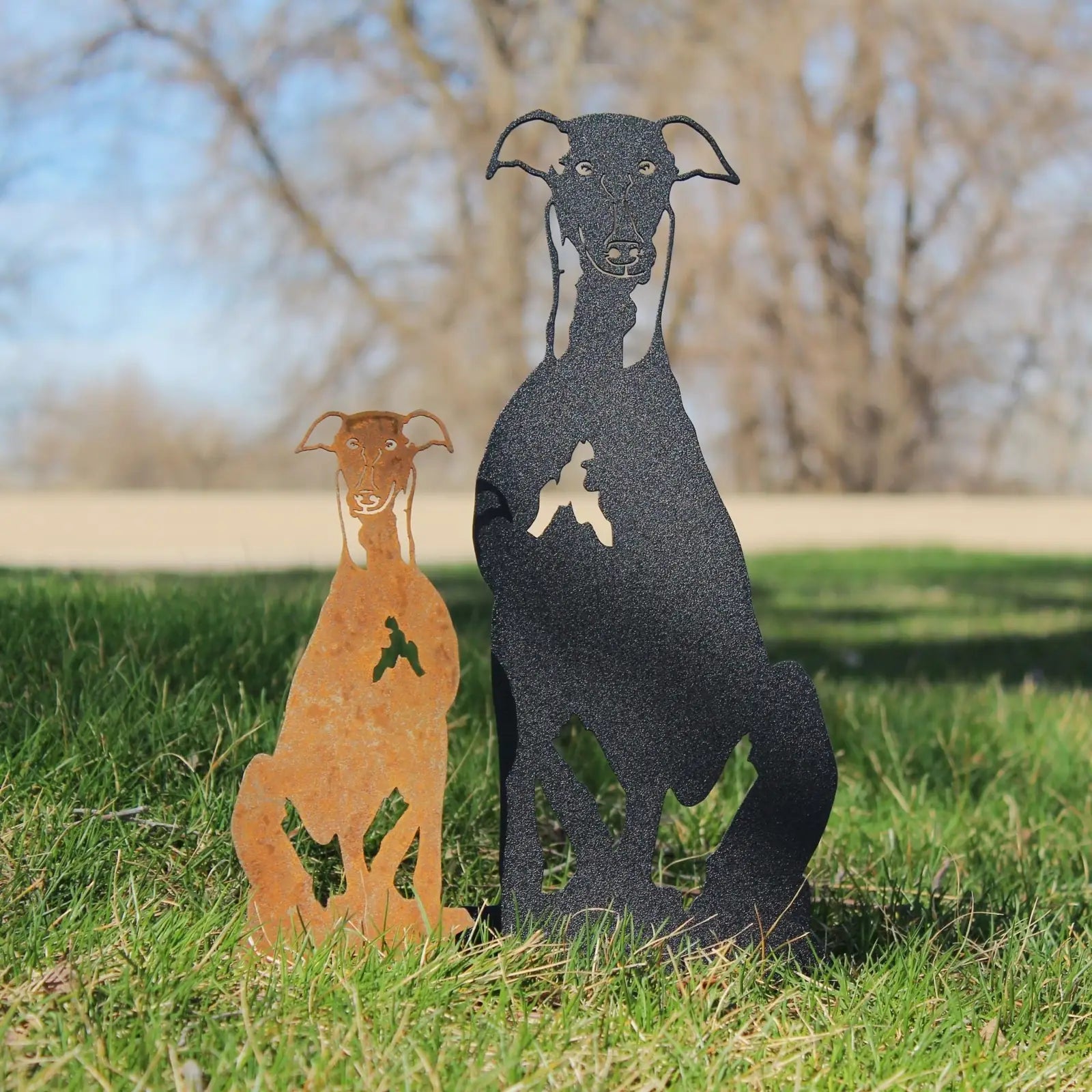 Whippet metal silhouette sculpture in black and rusted Corten steel, artfully displayed on green grass outdoors.